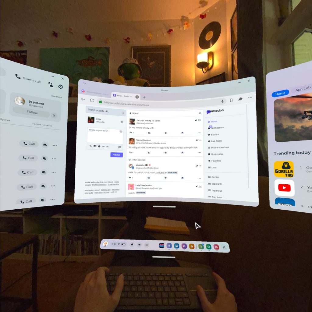 Riley sitting on a couch in her living room. Three virtual monitors surround her, with a single grey keyboard in her lap.