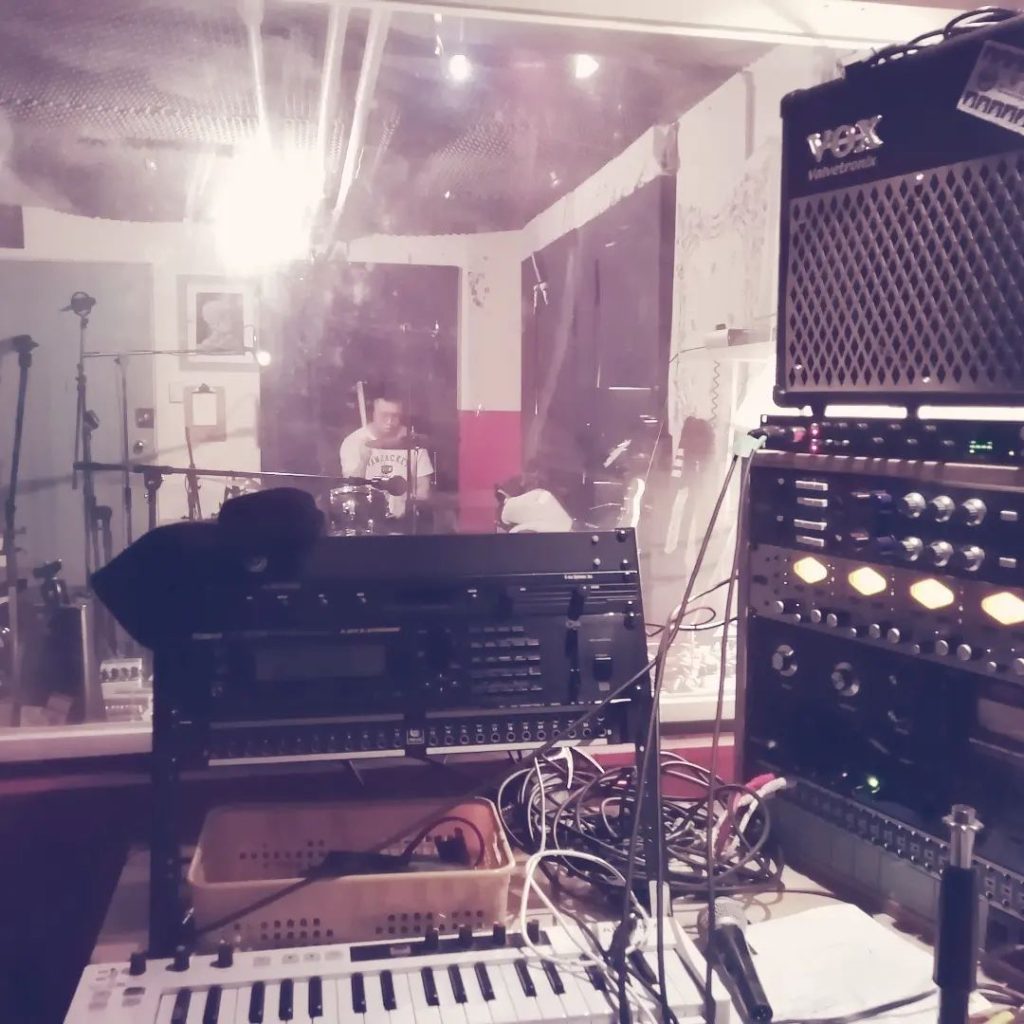 Peter Lee drumming in the CHOMS recording studio. On the desk in front of the camera is a wide variety of equipment used for recording purposes.