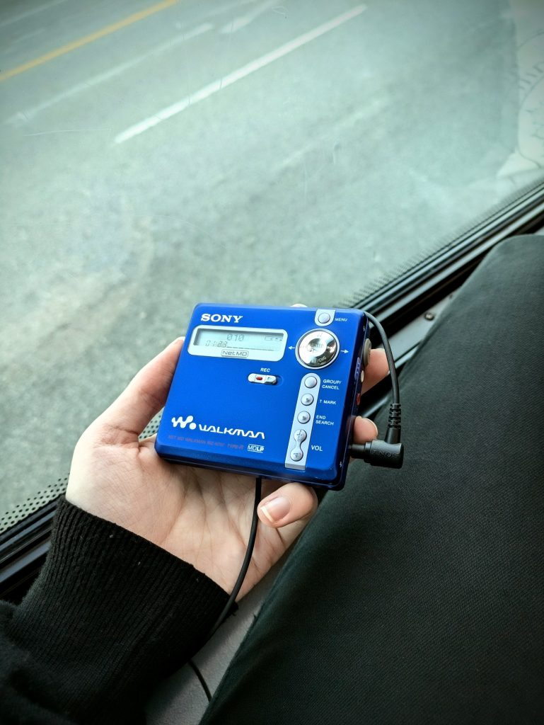 The blue Sony MZ-N707 MiniDisc player being held in Riley's hand on board a bus. 